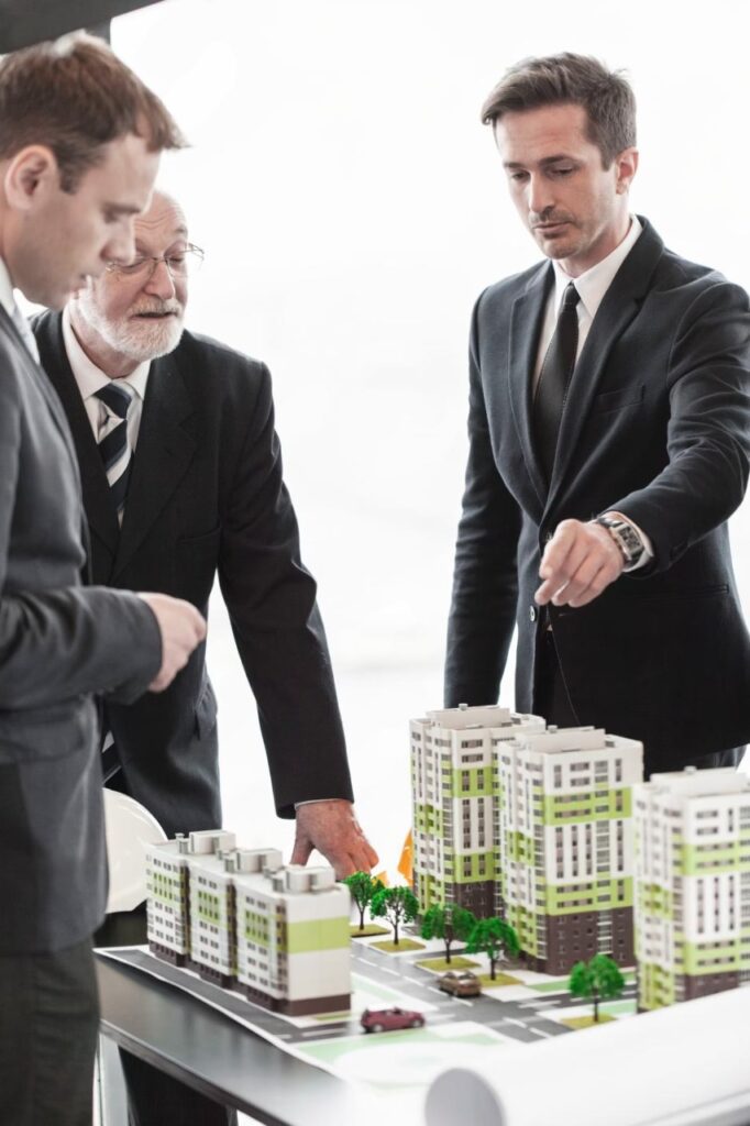 Real estate professionals discussing a model of a building at a meeting table.